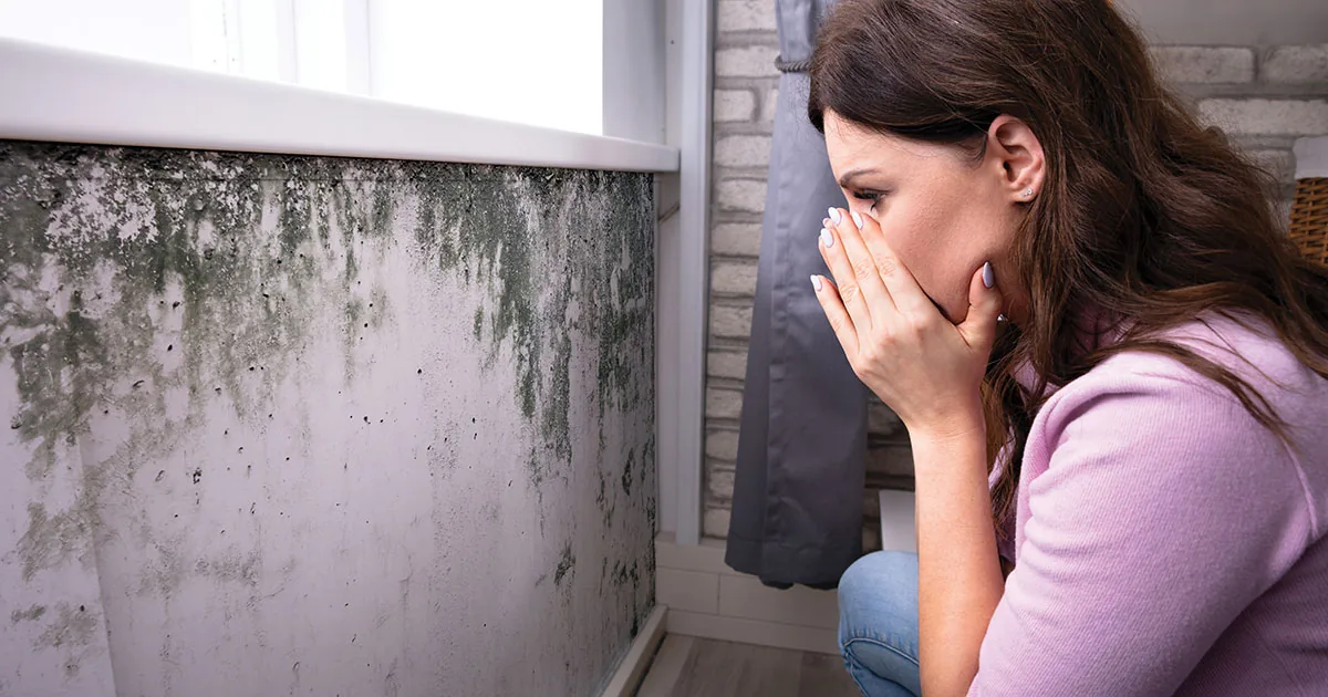 A woman covering her face beside a wall with heavy mold growth