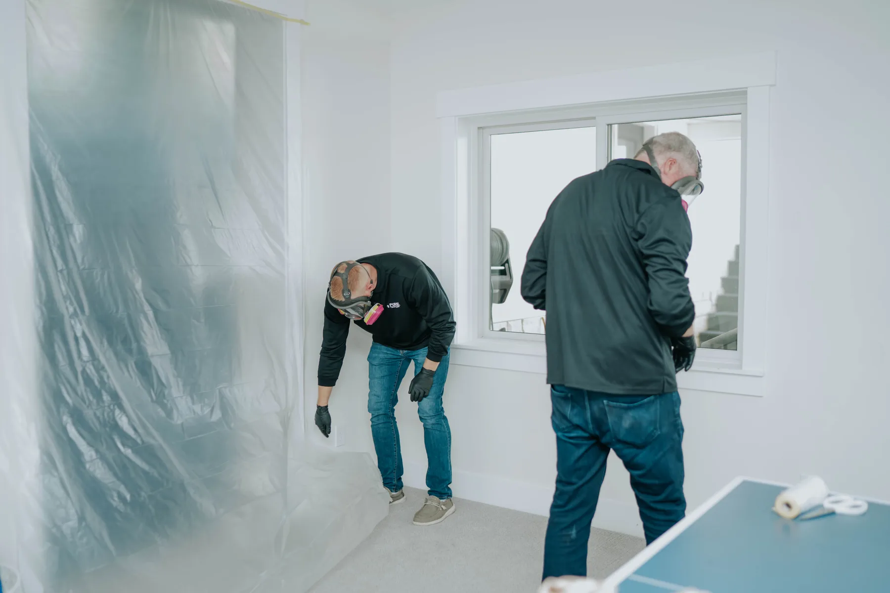 Two technicians working in a room sealed with plastic sheeting