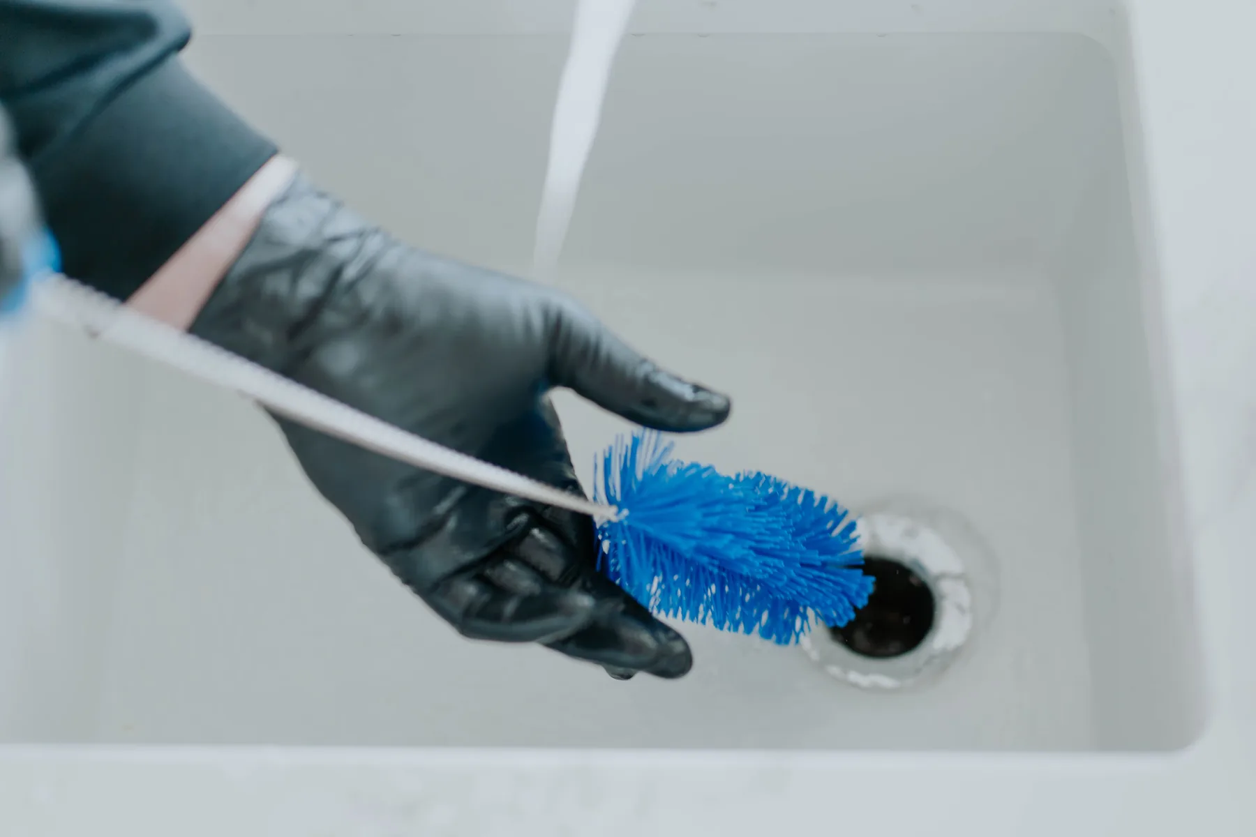 A gloved hand cleaning a sink drain with a brush